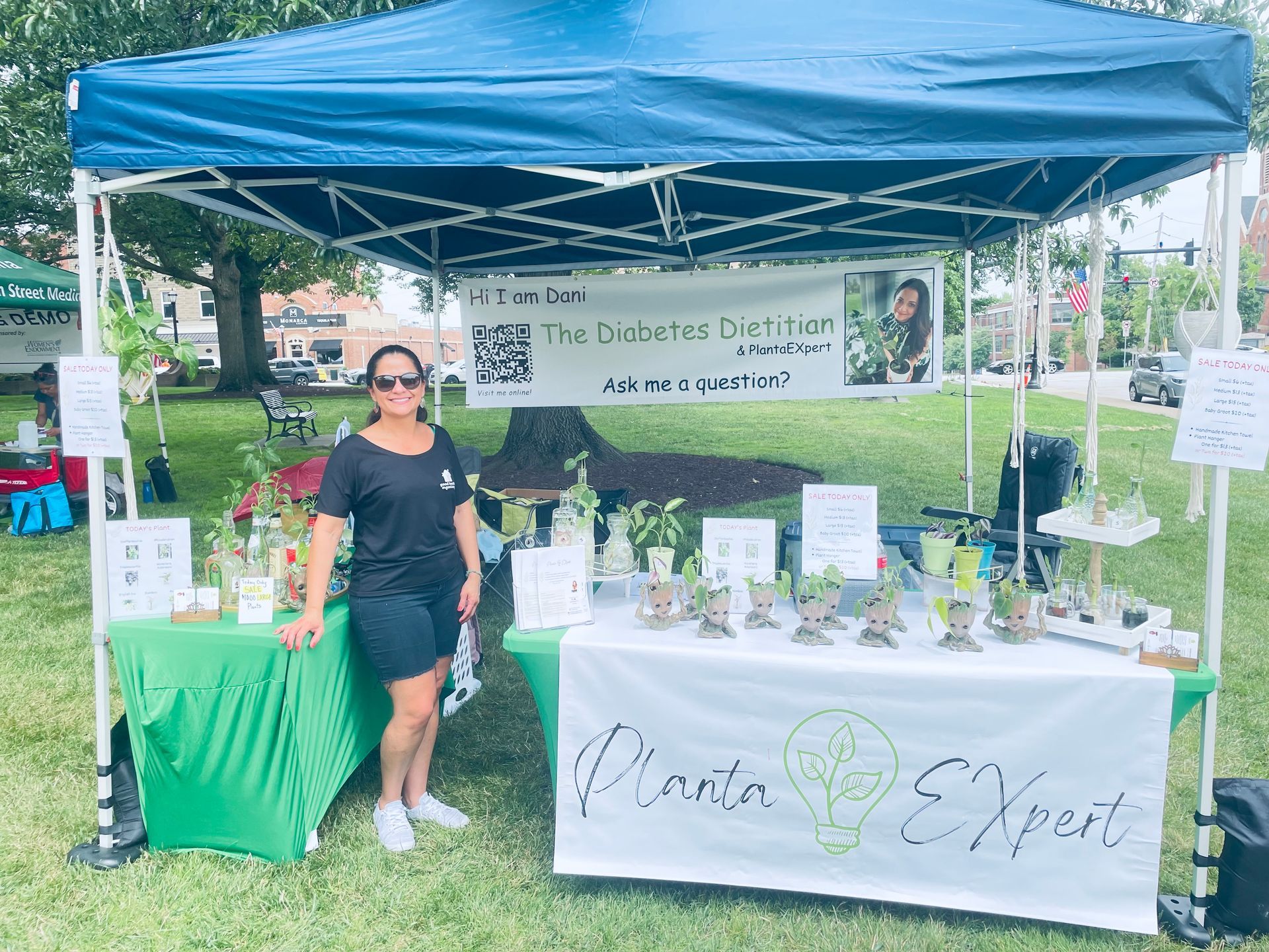 A woman is standing in front of a table under a tent at a farmers market.