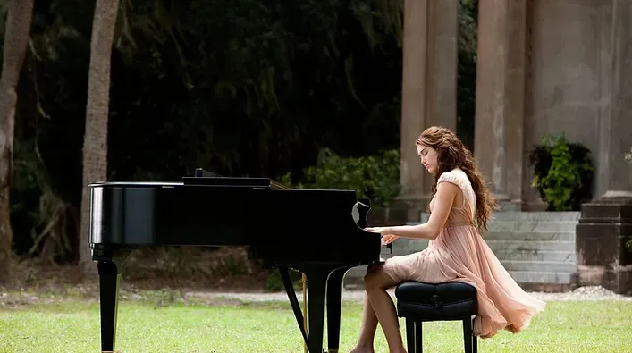 A woman in a pink dress is sitting on a bench playing a piano.