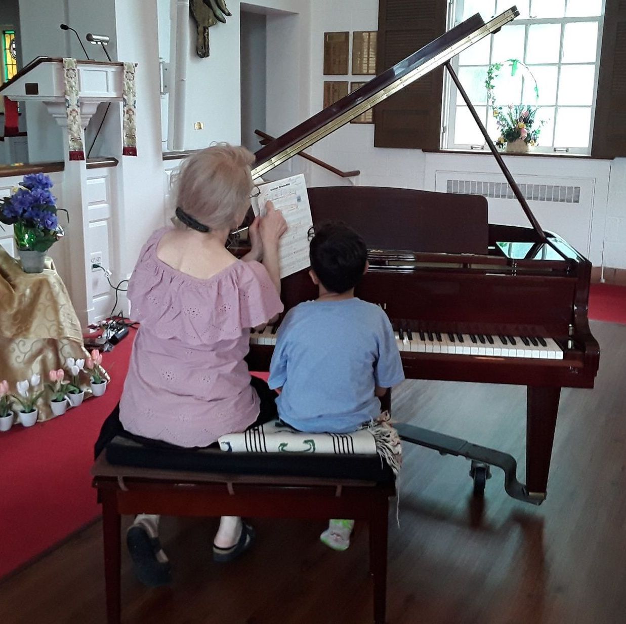 A woman sits on a bench next to a child playing a piano