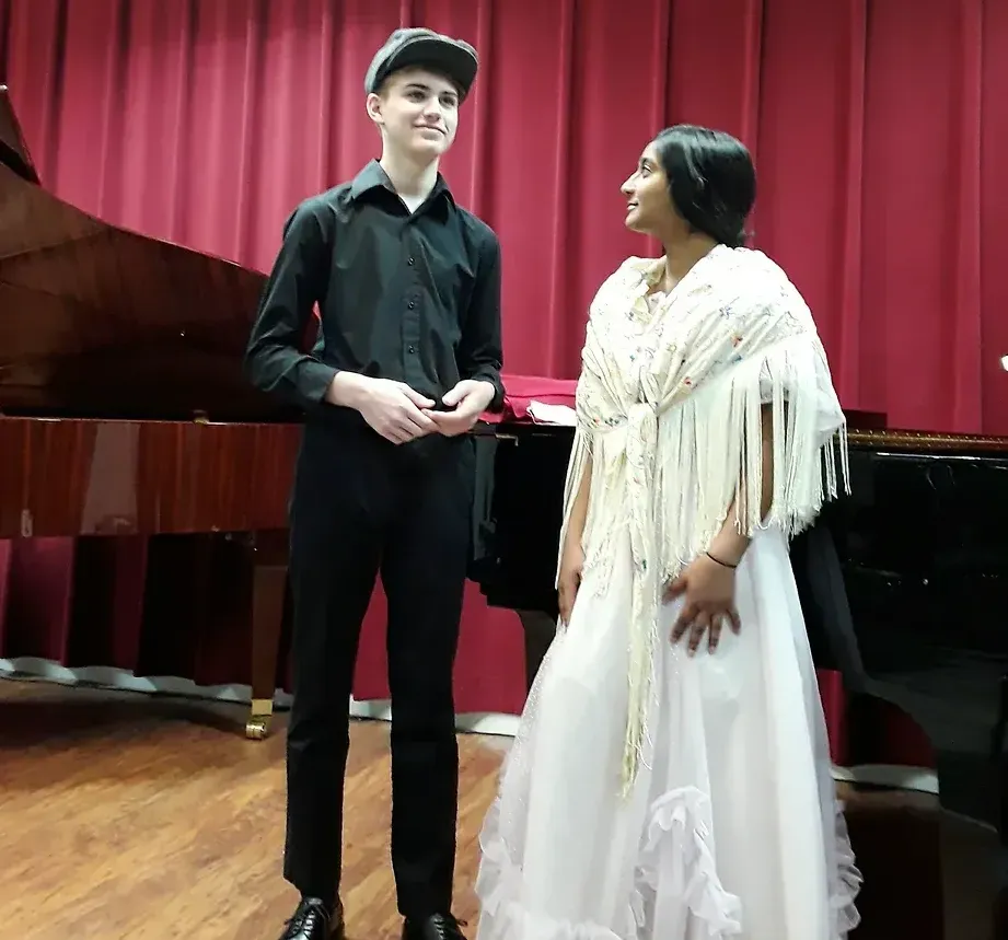 A man and a woman are standing next to each other in front of a piano
