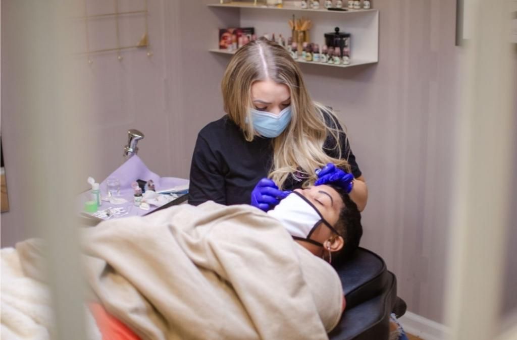 A woman wearing a mask is working on a man 's eyebrows.