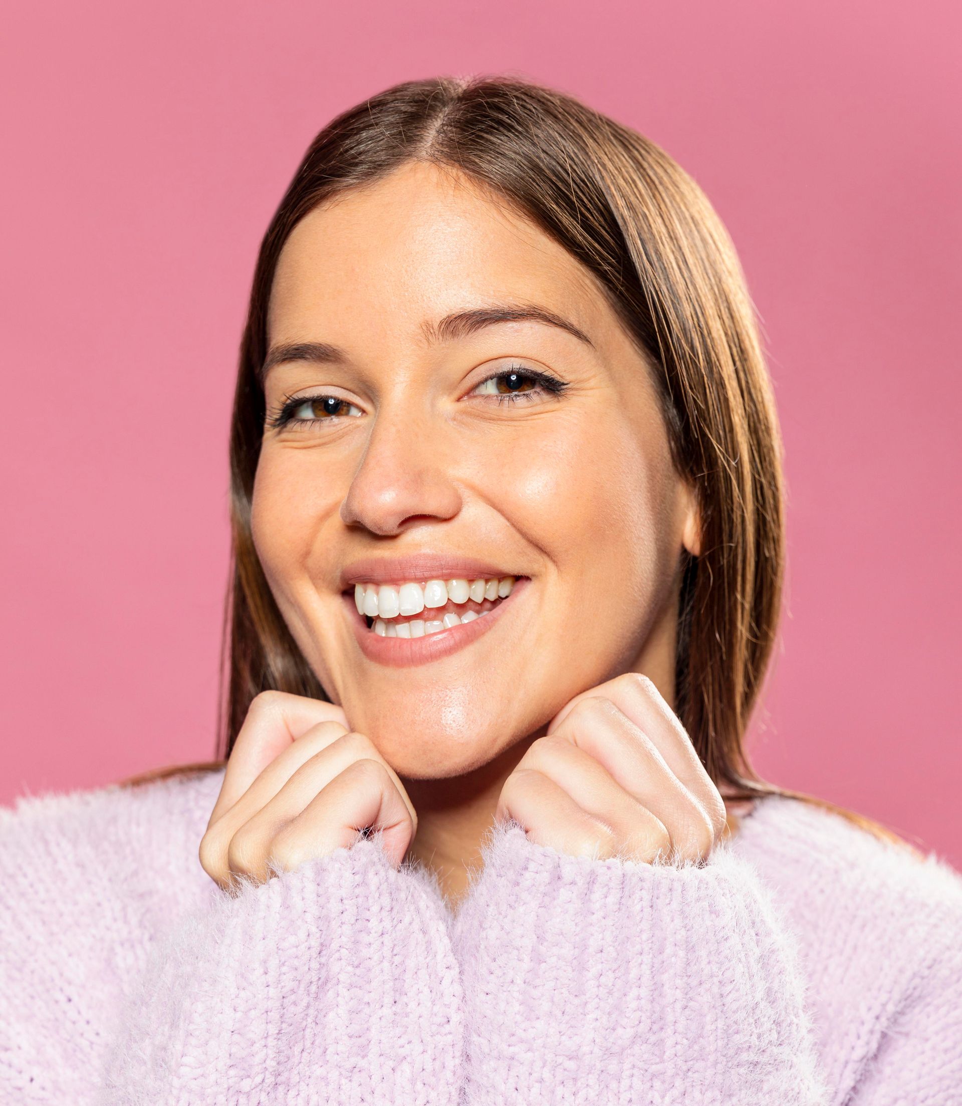 A woman in a purple sweater is smiling and holding her hands to her face.