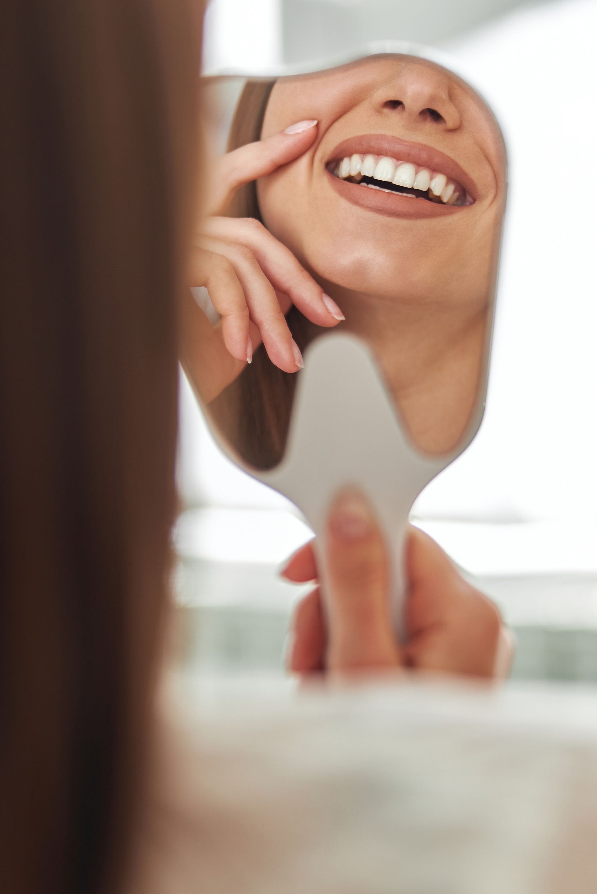 a woman looks at her smile in a hand mirror