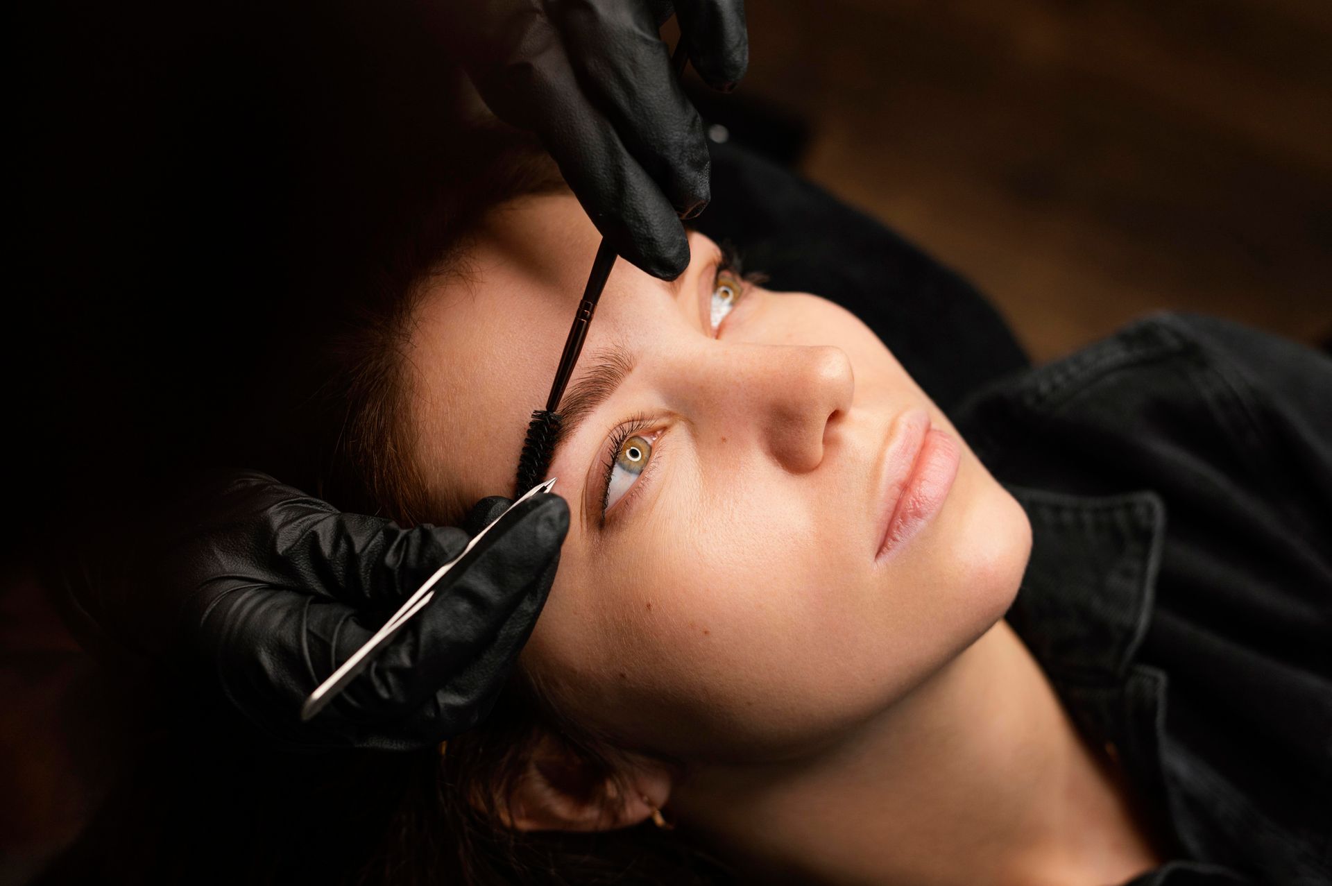 a woman is getting her eyebrows done by a person wearing black gloves