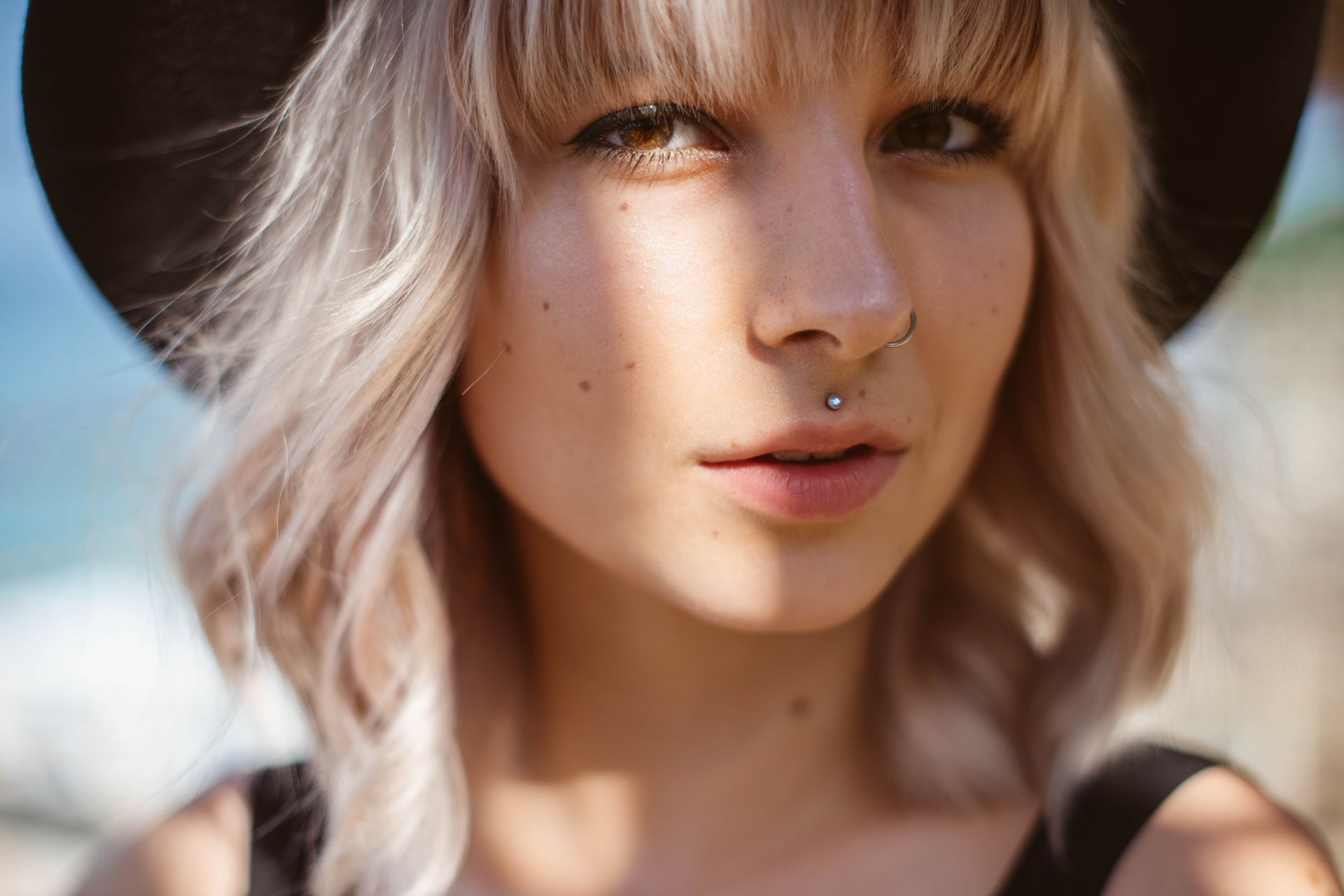 A close up of a woman wearing a hat and a nose ring.