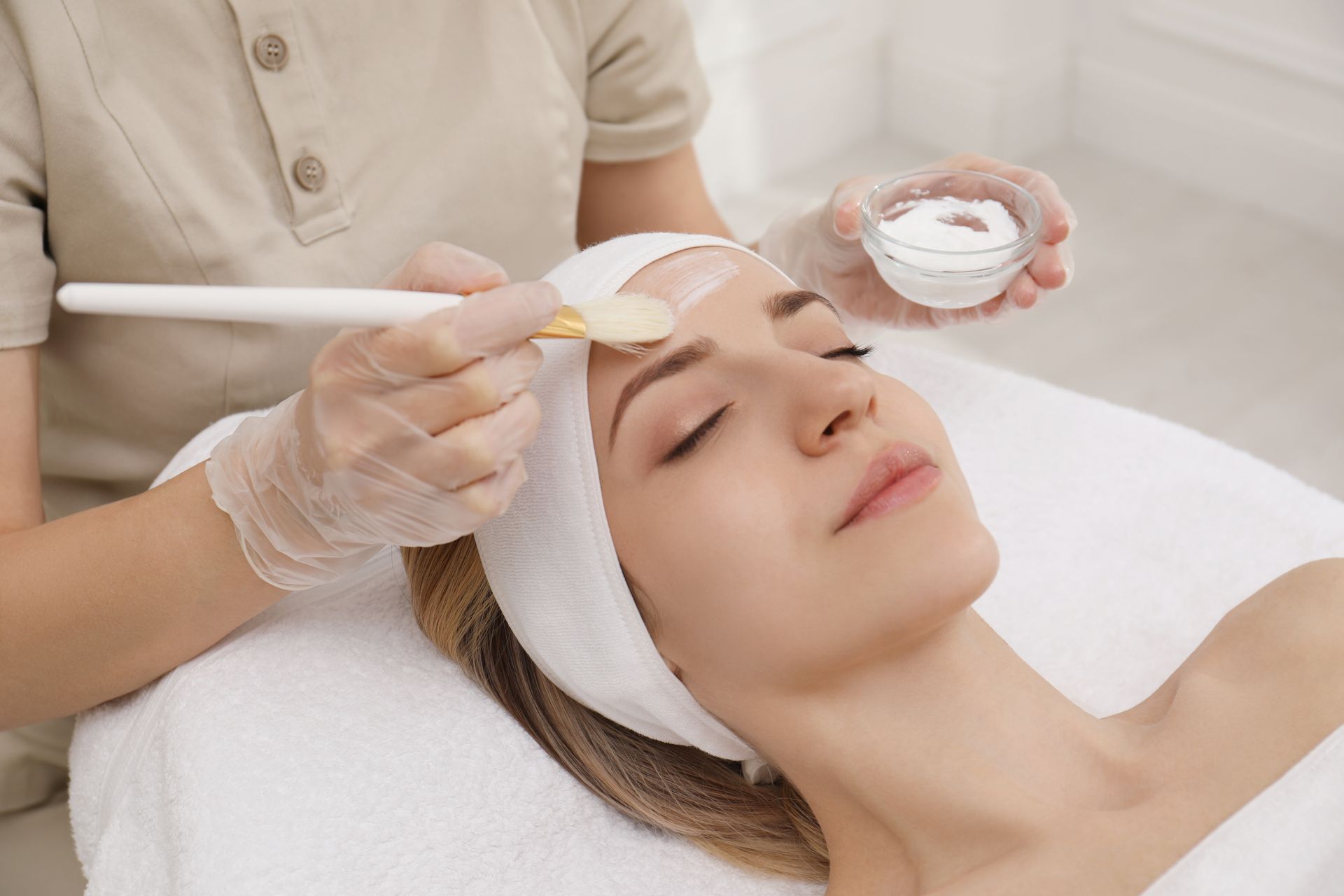 Woman receiving a facial mask treatment at a spa. The esthetician applies mask to her forehead.