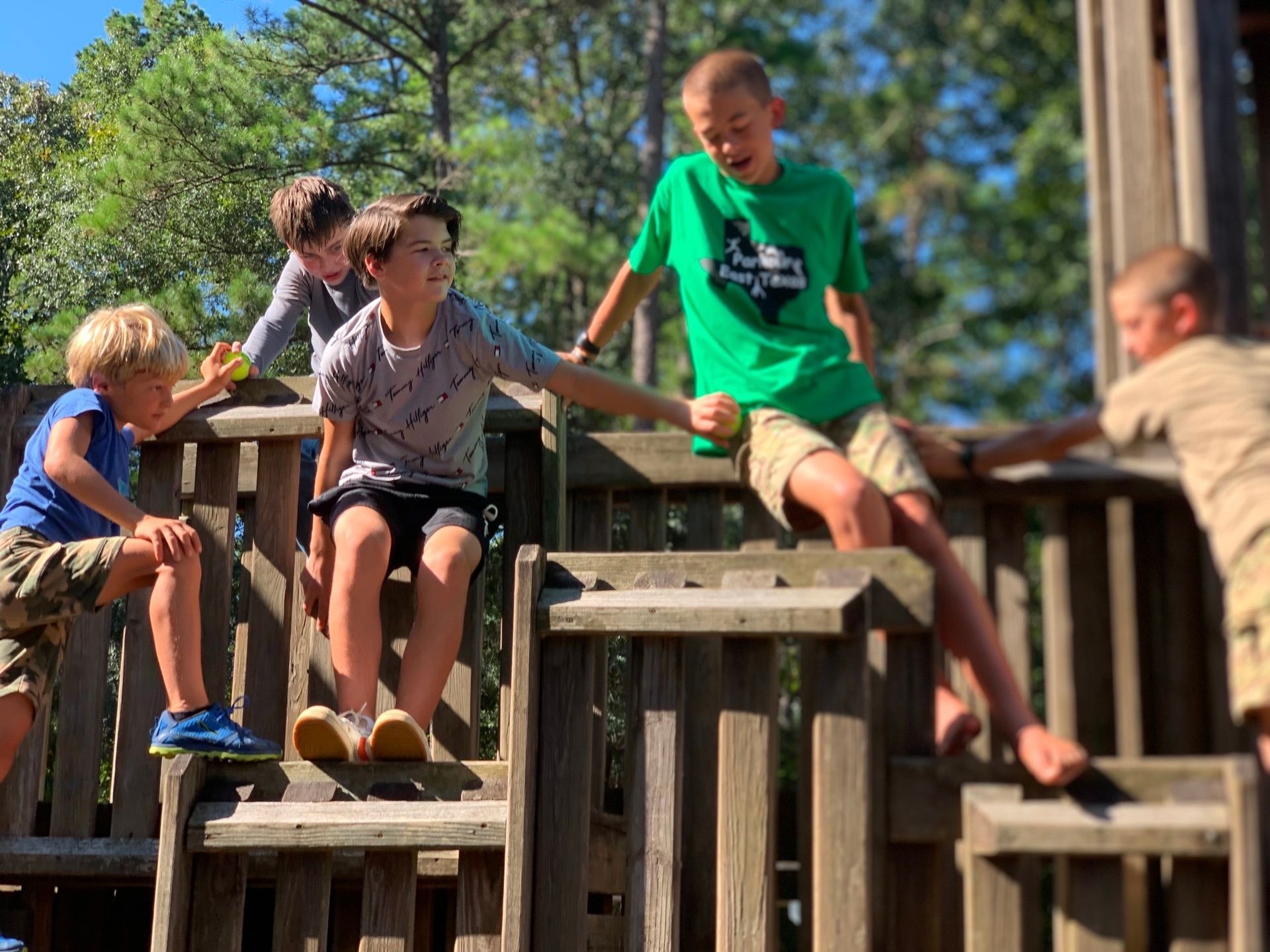 A group of young boys are playing on a wooden playground.
