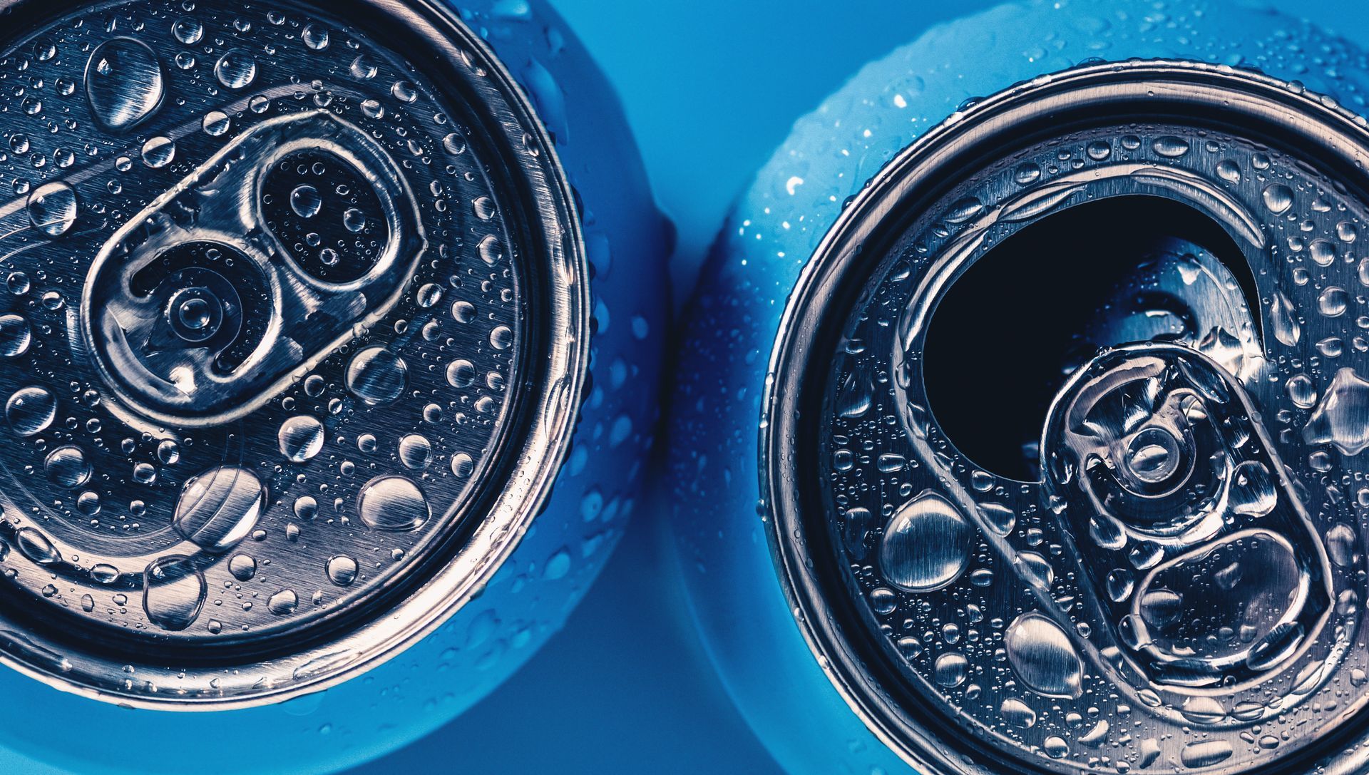 Top view of two opened soda cans with blue tab tops and condensation droplets on a blue background