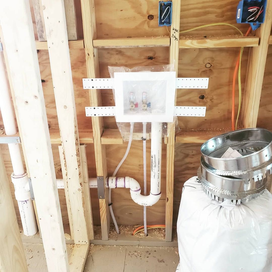 Laundry room plumbing rough-in. White washer box, pipes, and vent in wooden wall framing.