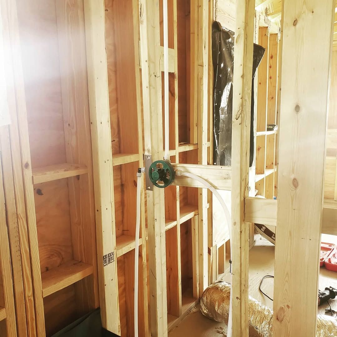 Interior view of a wooden framed structure with plumbing fixtures installed during construction.