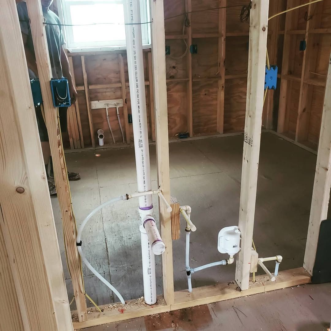 Interior of a room under construction with exposed wooden framing, plumbing, and electrical boxes.