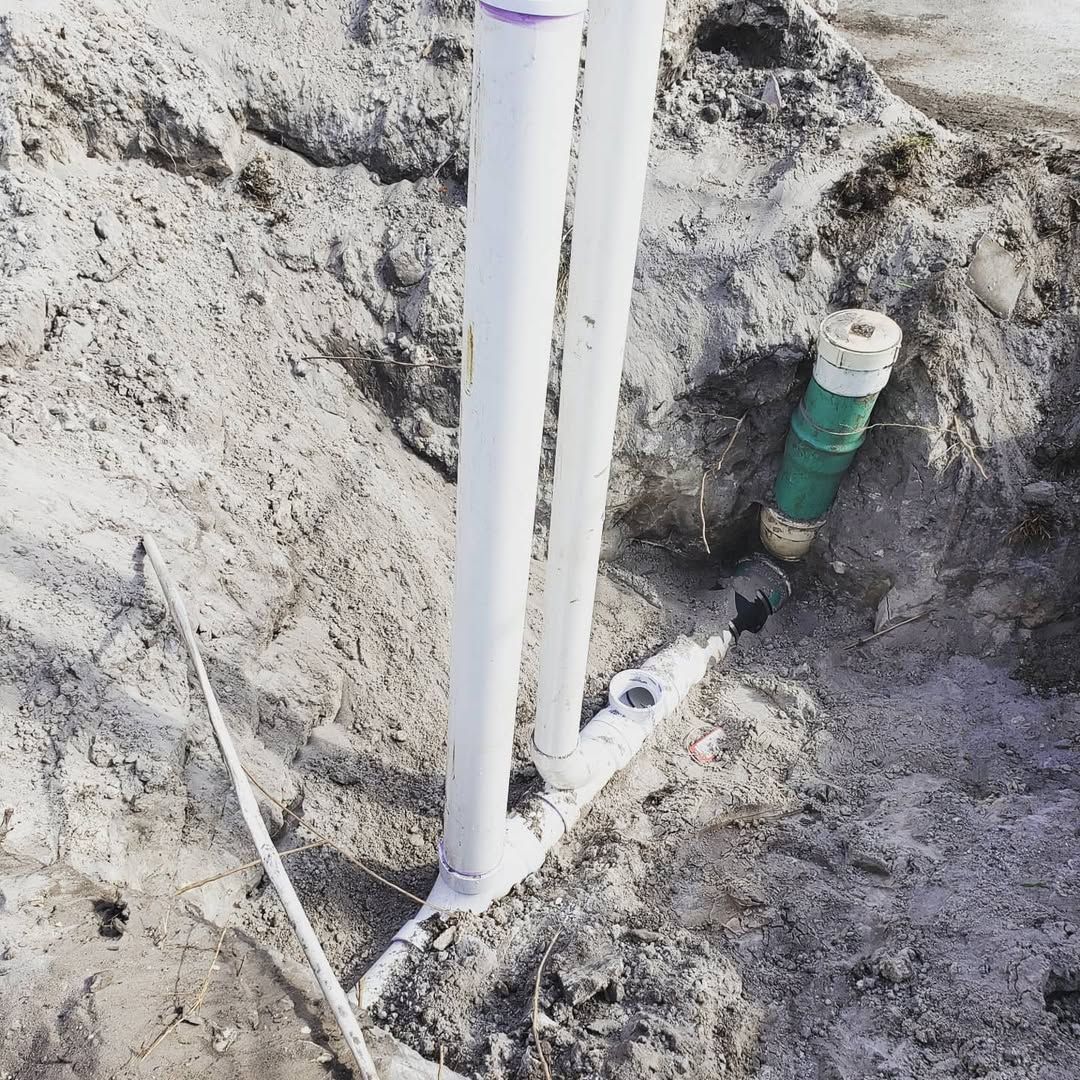 White PVC pipes in a dirt hole connected to a green pipe.