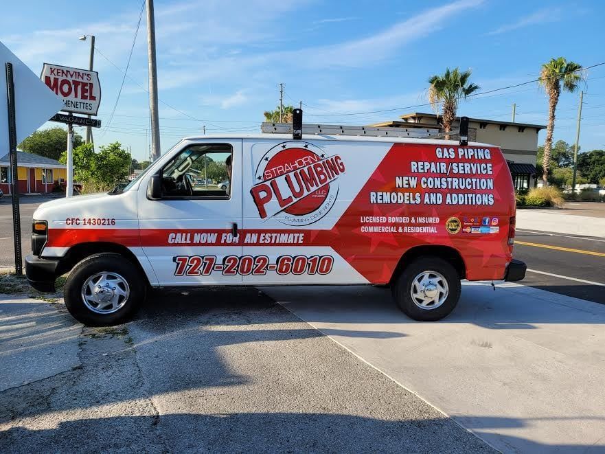 White plumbing van with red accents parked near a motel sign, advertising services like repair and new construction.