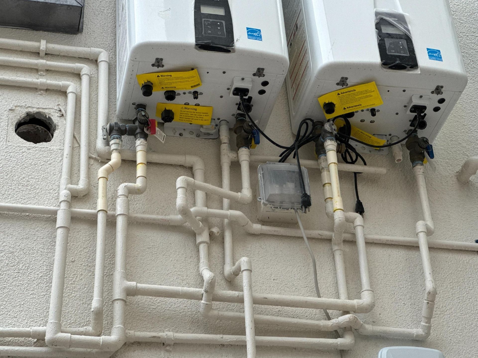 Two white water heaters mounted on a wall with white PVC pipes connecting them.