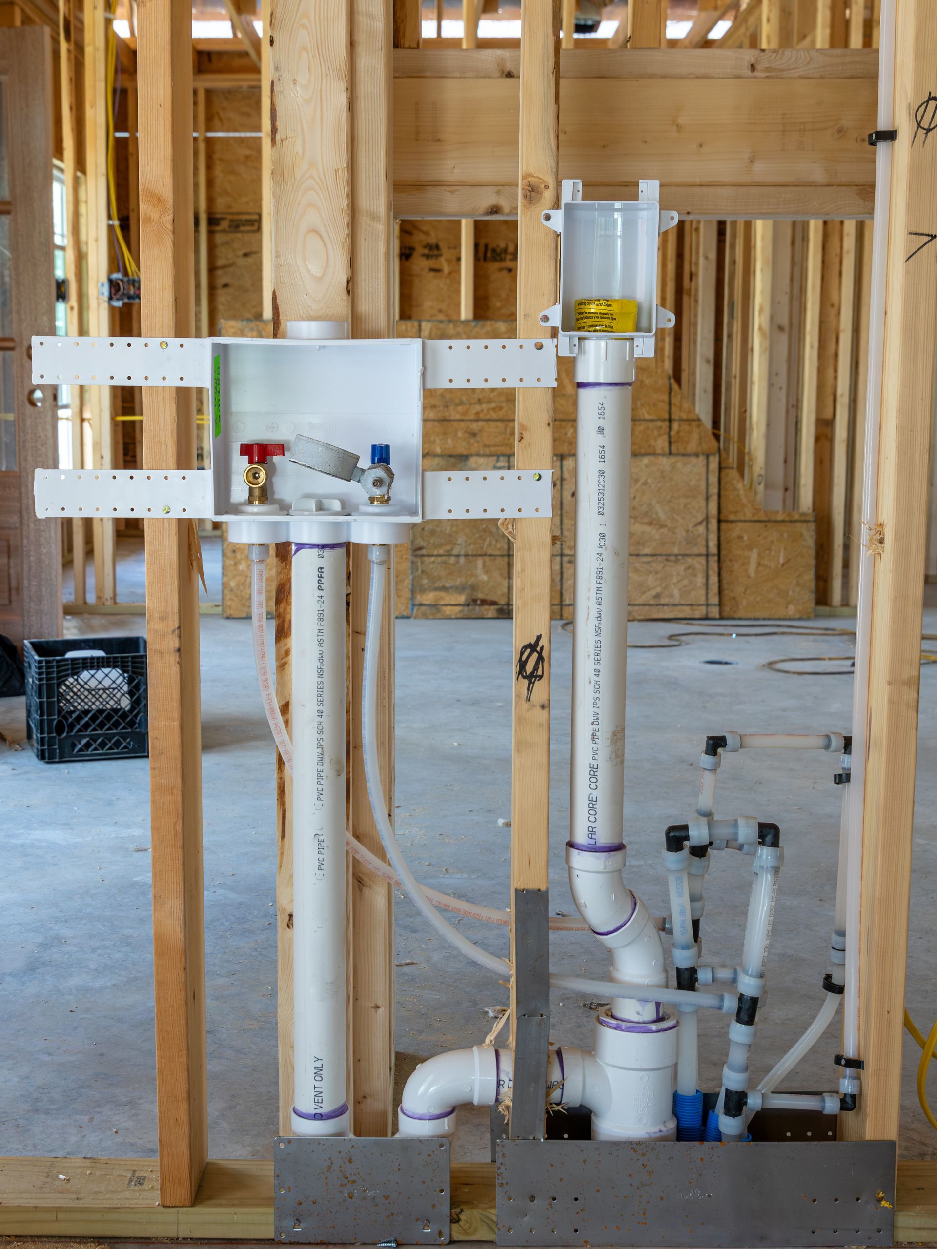 Framed laundry room plumbing with water lines and drain pipes visible, construction setting.