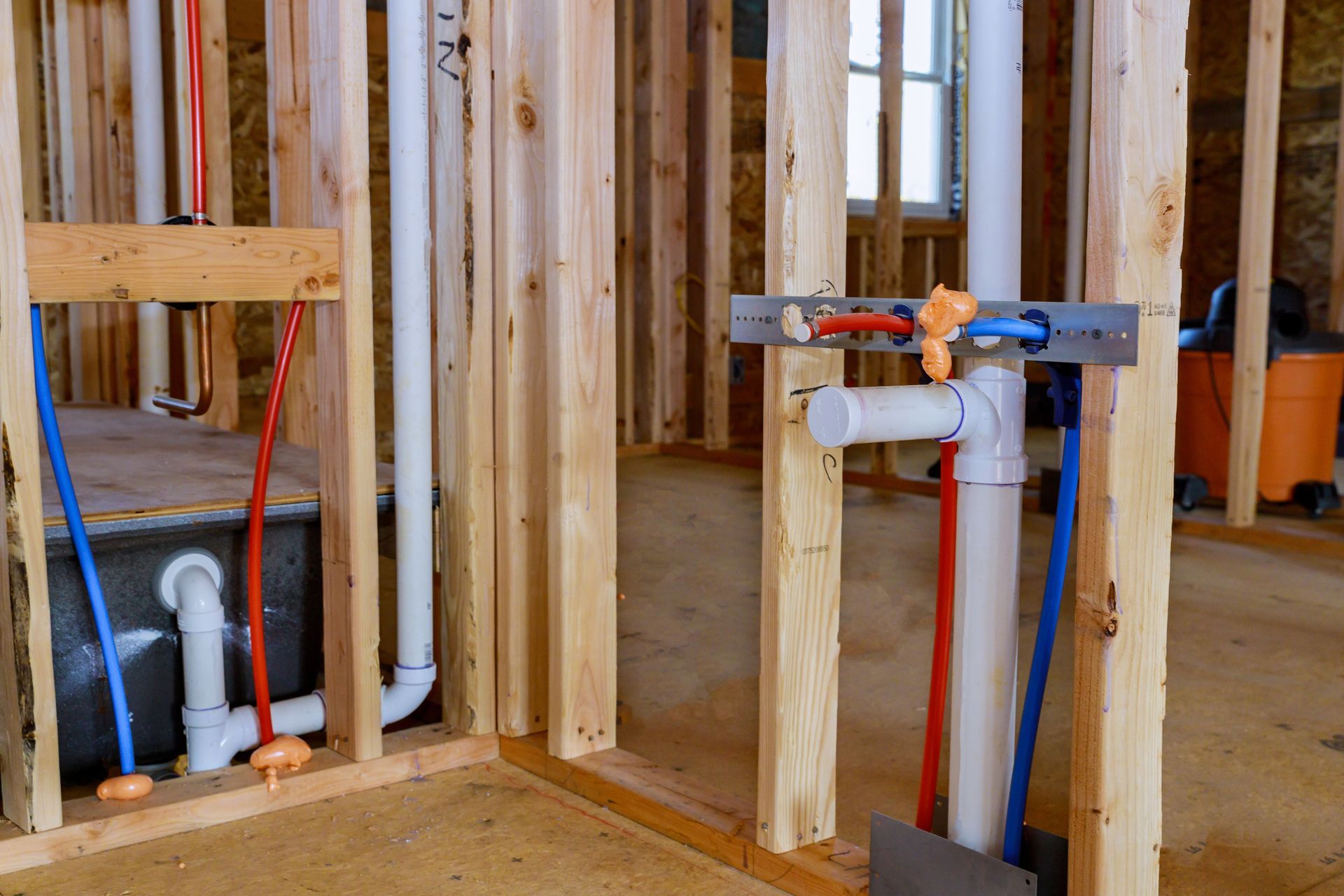 Interior view of a wooden framed wall with plumbing pipes, red and blue, for a new build.