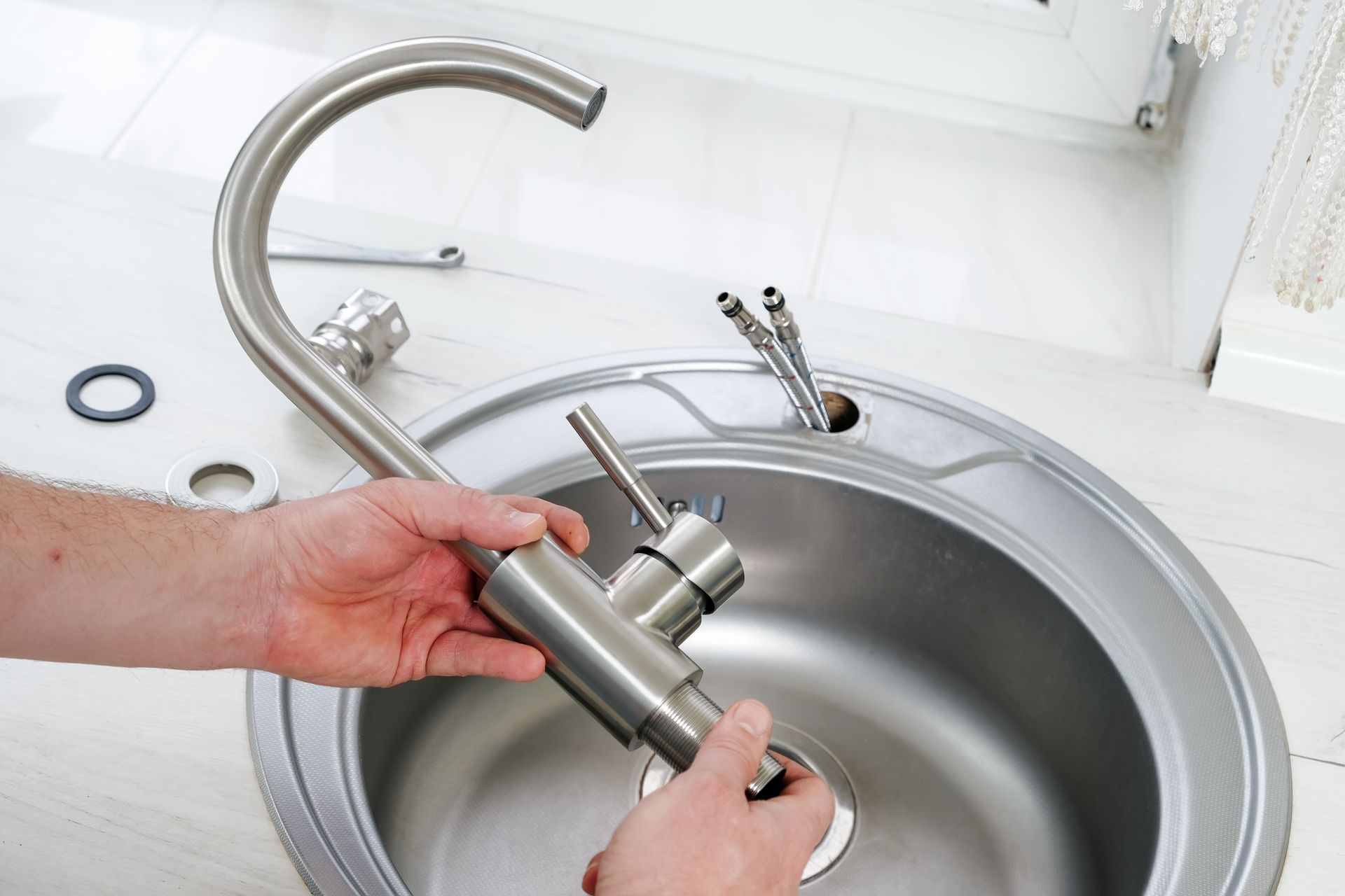 Hands installing a silver kitchen faucet in a stainless steel sink.