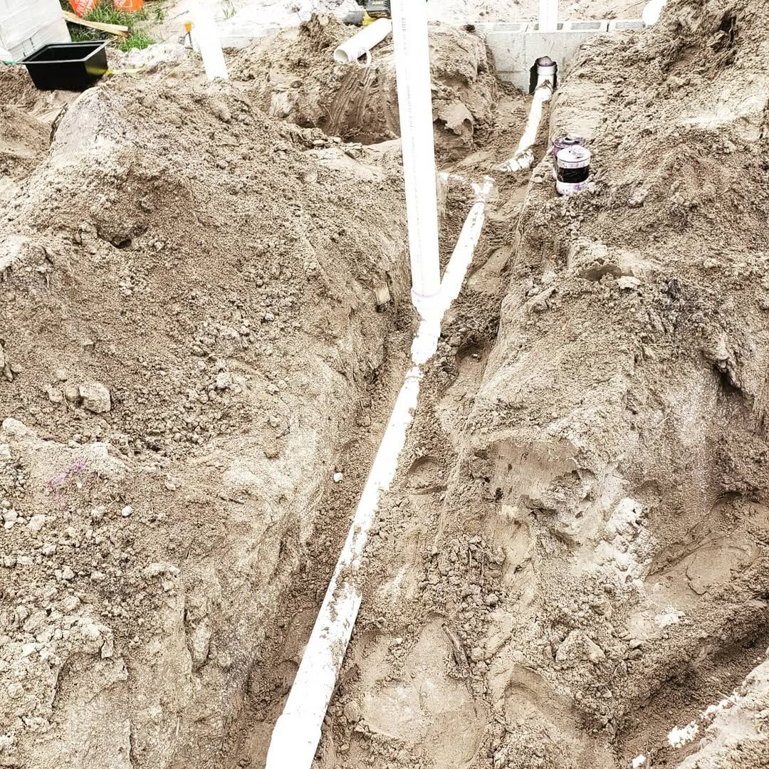 Excavated trench with white PVC pipes, construction site.