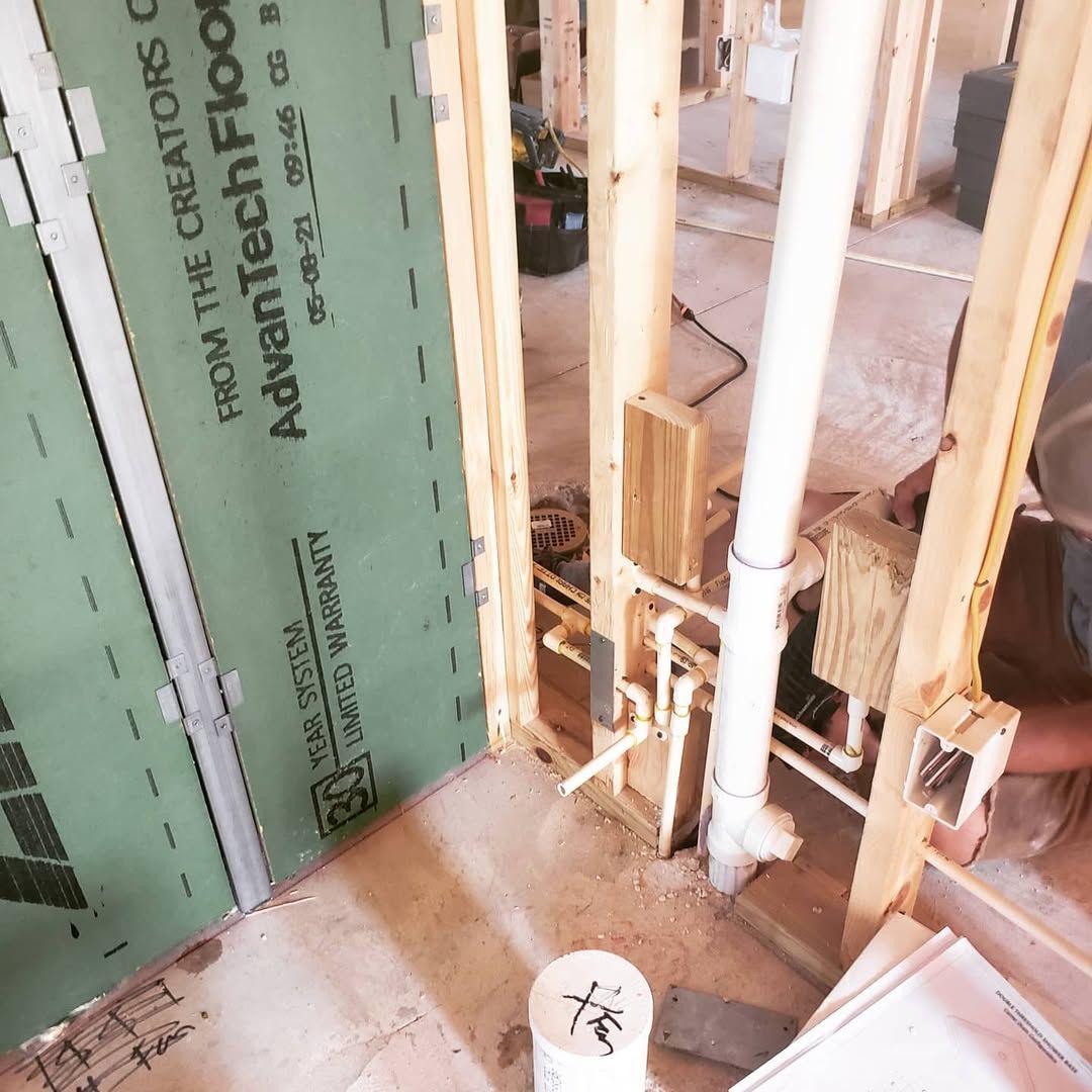 Framed walls with plumbing. Green wallboard and a worker visible in a construction setting.
