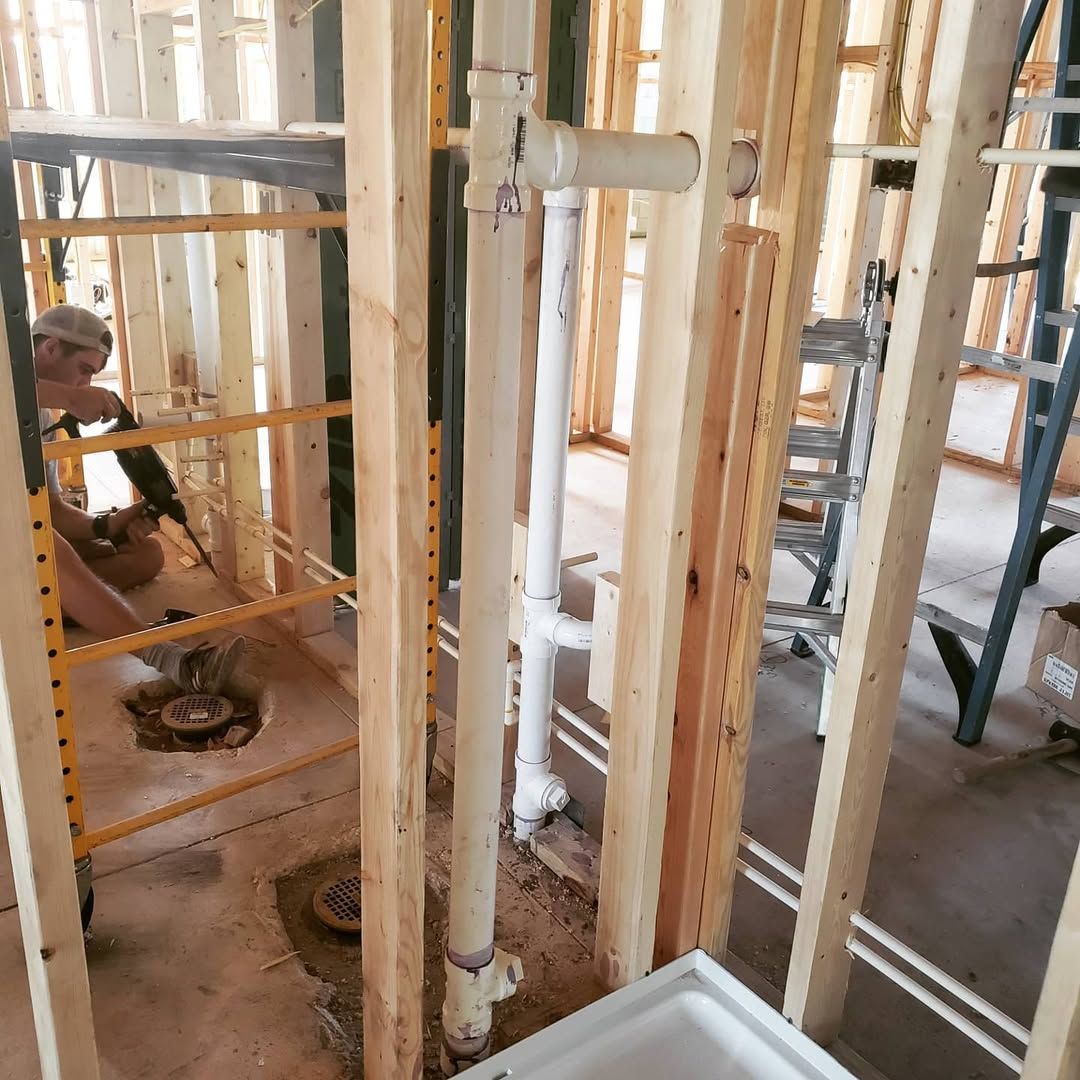 Construction site with plumbing pipes and a person working on the structure with a tool.