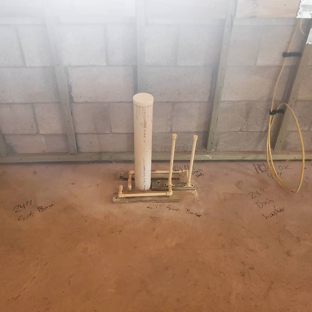 Plumbing rough-in for a toilet, pipes on concrete floor against a cinder block wall.