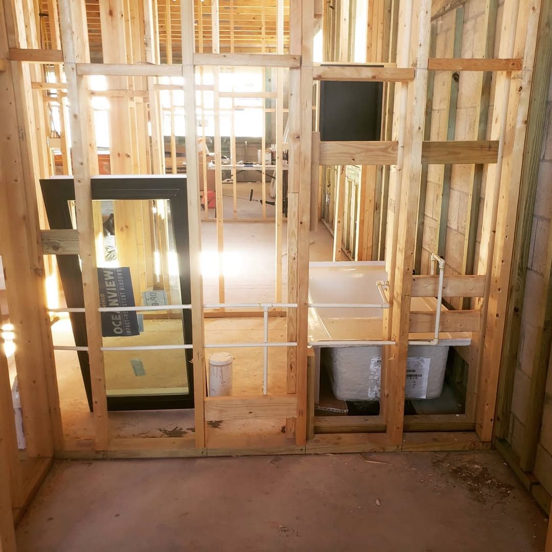 Bathroom under construction. Wood framing with openings for a mirror, sink, and shower. Daylight streams in.