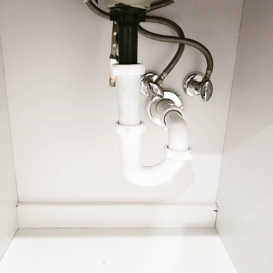 White bathroom sink plumbing, with visible p-trap and supply lines, under a white cabinet.