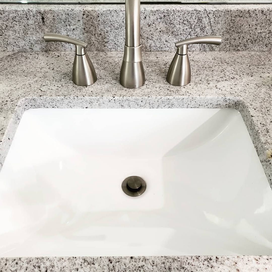 White bathroom sink with silver faucet and handles, set in speckled countertop.