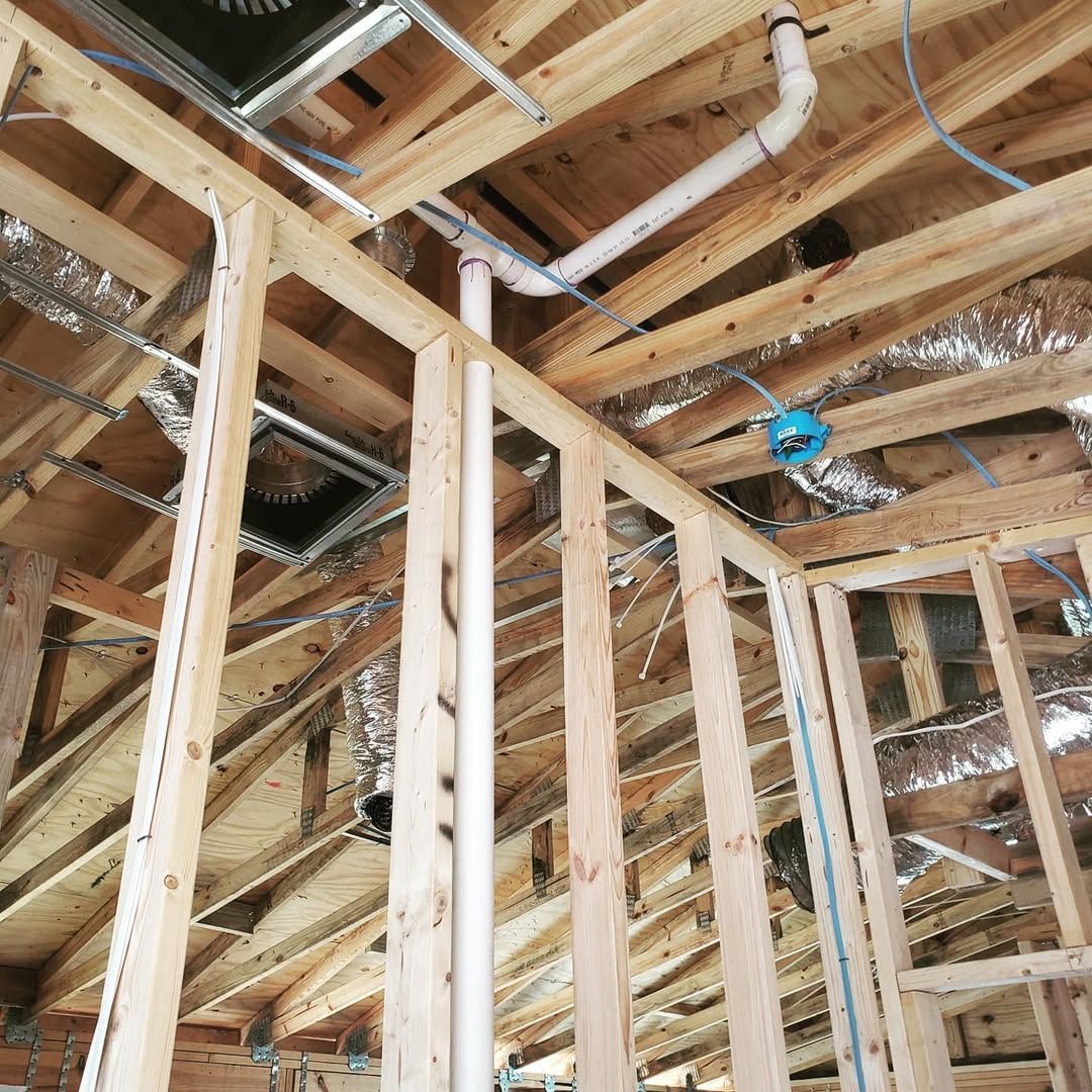 Wooden framework of a building's interior showing exposed plumbing and electrical work in the ceiling.