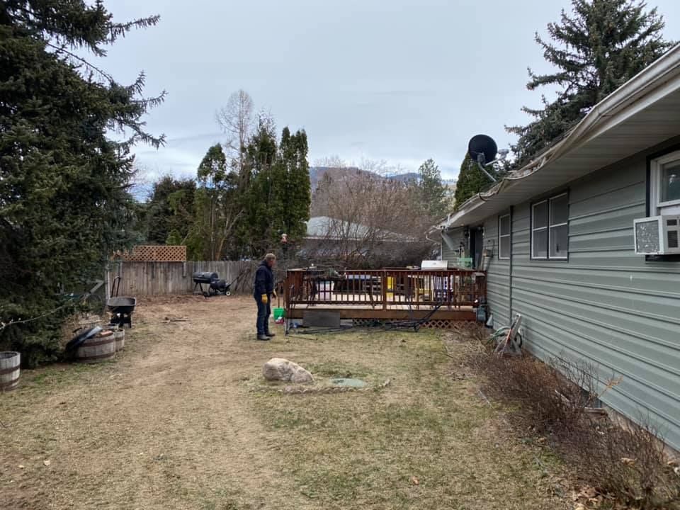 Backyard with a person standing on the lawn near a wooden deck and house with a green exterior. Overcast day.