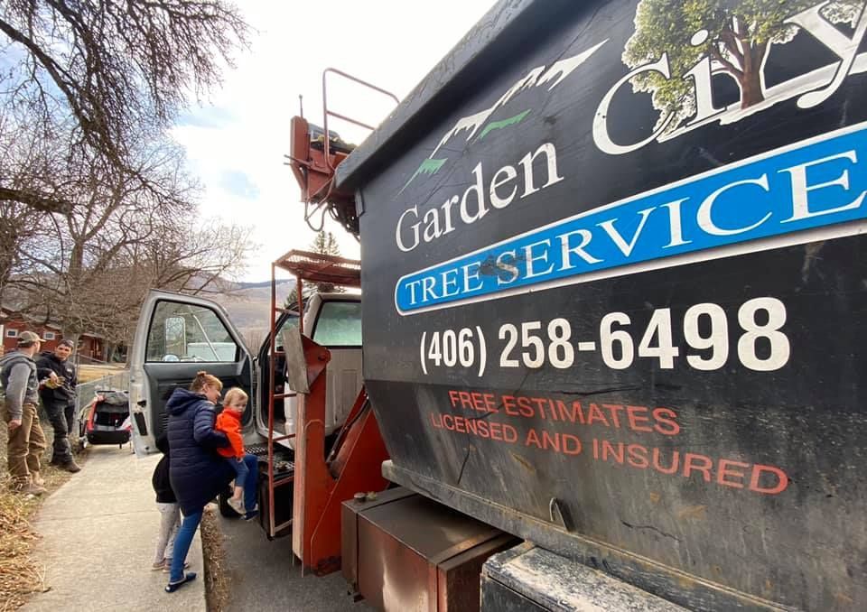 A Garden City Tree Service truck with the phone number (406) 258-6498. People are standing near the truck.