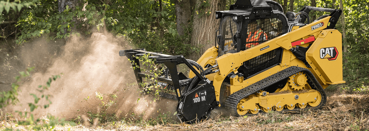 A yellow Caterpillar forestry mulcher clearing brush and creating a cloud of dust in a wooded area.