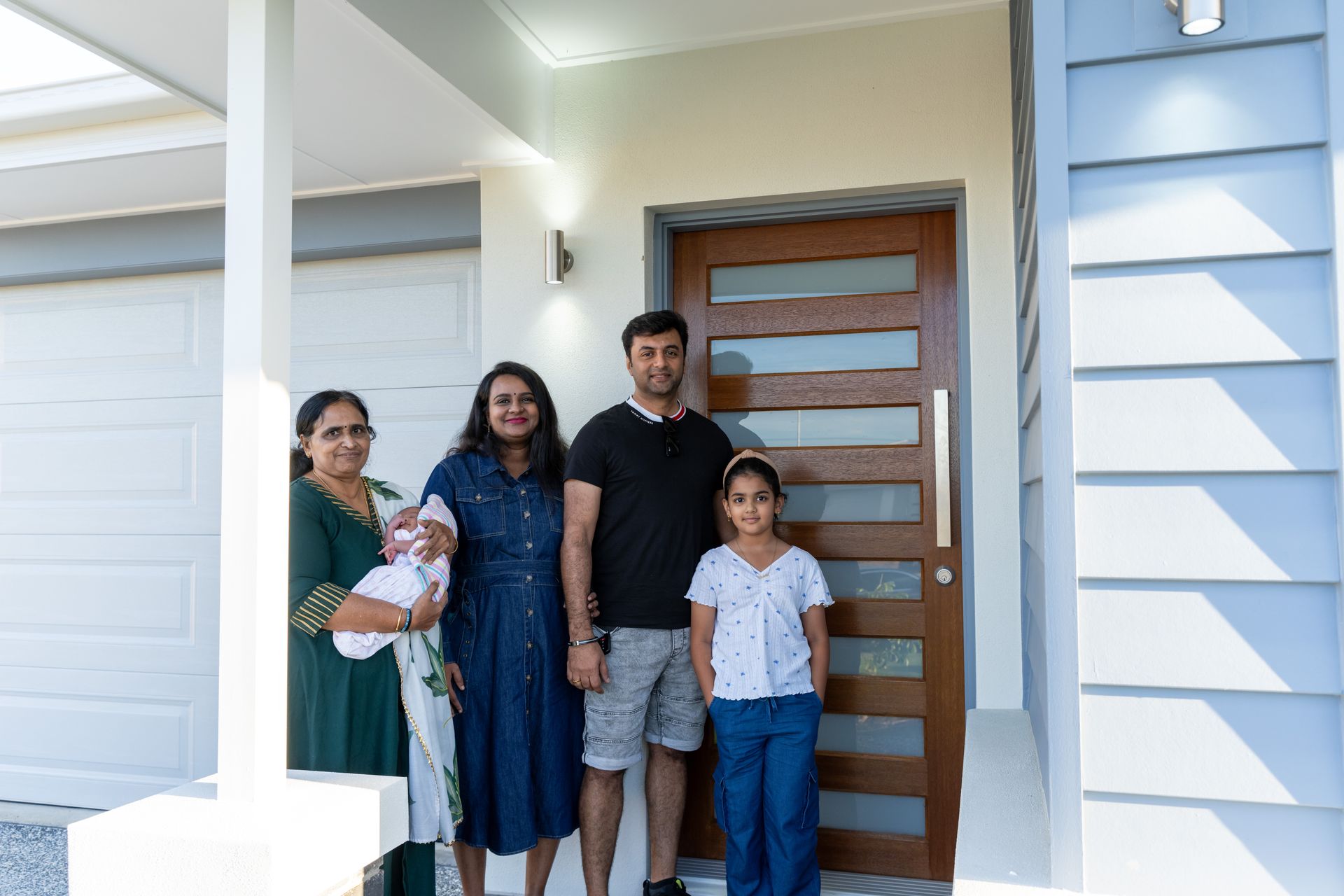 White suburban house with gray roof and garage door. Blue sky, green grass.