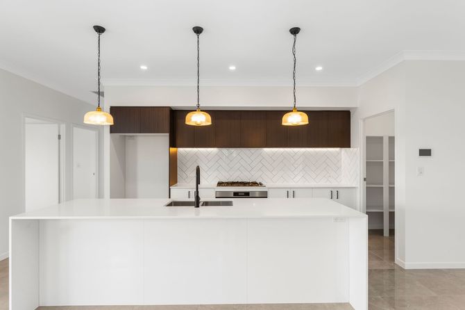 Modern kitchen with white island, dark cabinets, and three hanging gold lights.