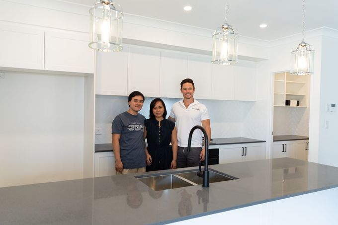 Three people smiling in a bright white kitchen with a gray countertop and black faucet.