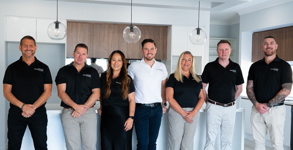 Seven people, standing in a kitchen, smiling and posing for a photo.