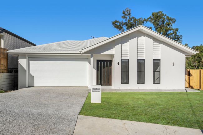 Modern home with white facade, stone accent, and sloping roof. Green lawn with landscaping.