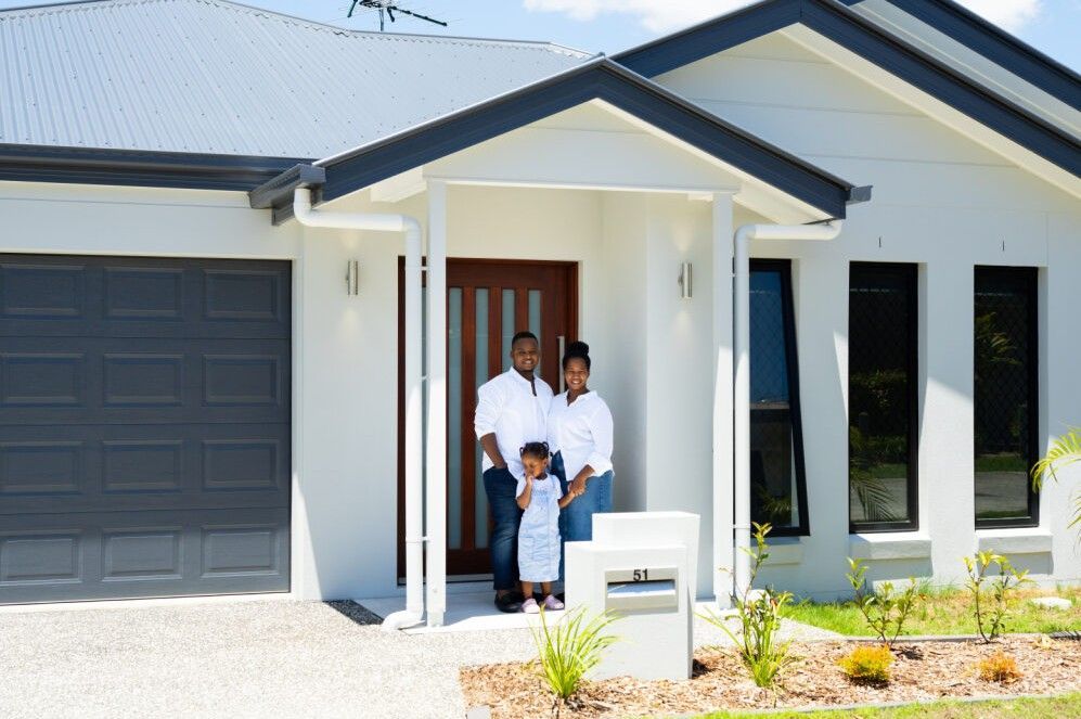 Single-story house with a white roof, gray siding, brown garage door, and a stone walkway.