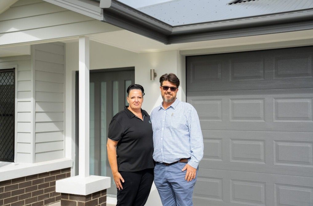 Single-story house with a white roof, gray siding, brown garage door, and a stone walkway.
