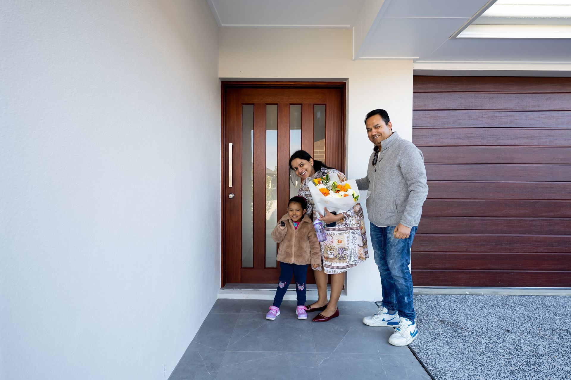 Single-story house with a white roof, gray siding, brown garage door, and a stone walkway.