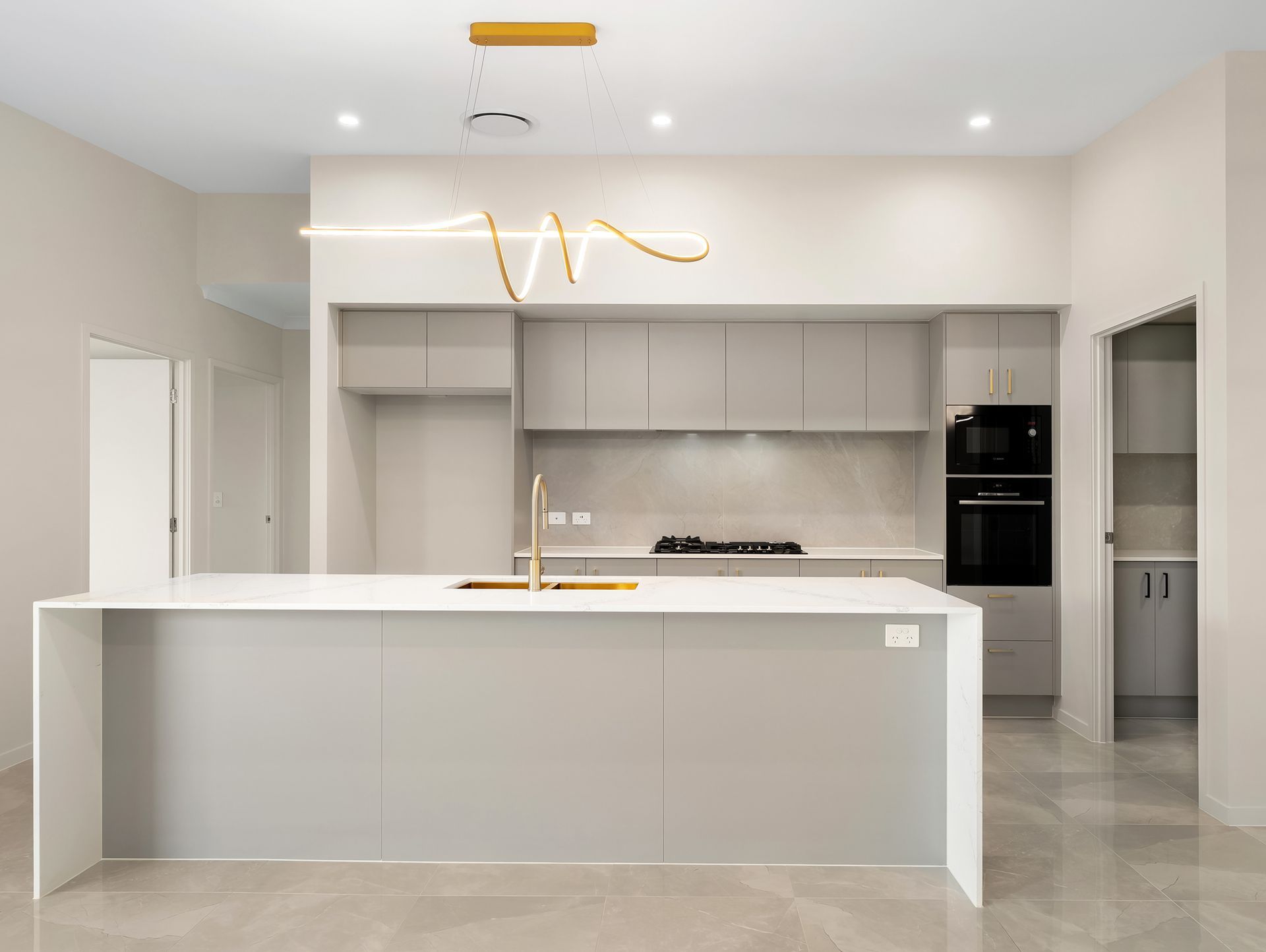 Modern kitchen with white island, dark cabinets, and three hanging gold lights.