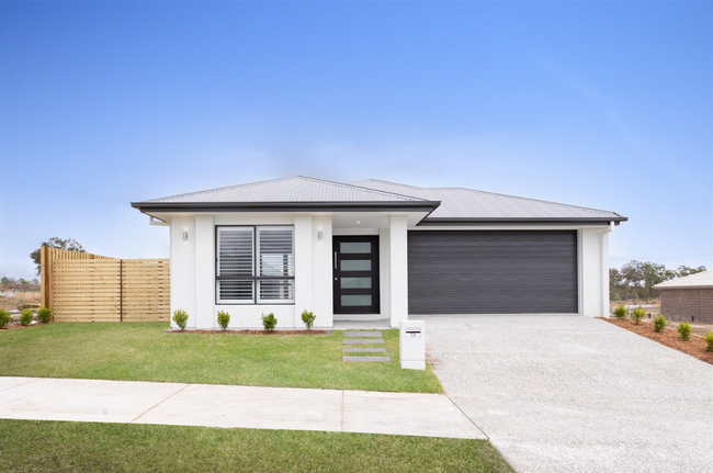 White suburban house with gray roof and garage door. Blue sky, green grass.