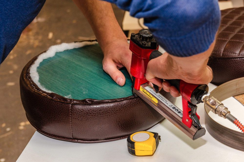 A Person is Using a Stapler to Fix a Chair Seat — Custom Unique Trimming in Mackay, QLD