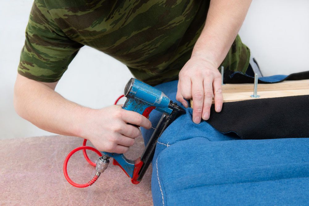 A Man is Using a Stapler to Fix a Piece of Furniture — Custom Unique Trimming in Mackay, QLD
