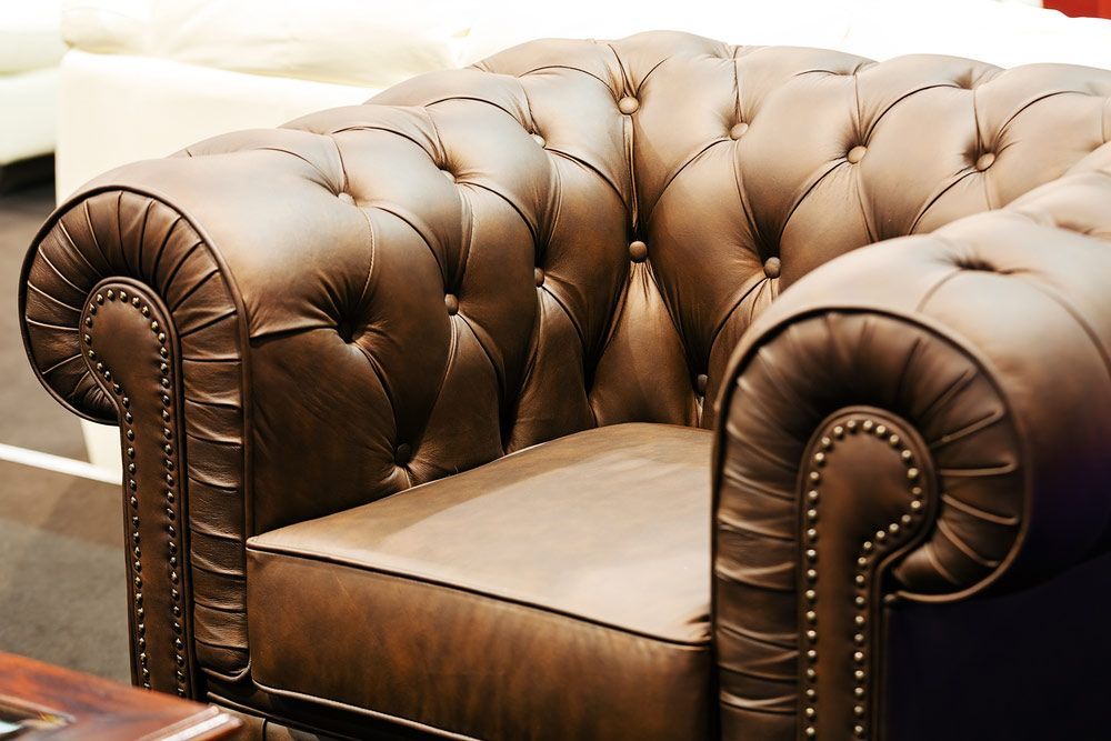 A Brown Leather Chair is Sitting Next to a Wooden Table — Custom Unique Trimming in Mackay, QLD