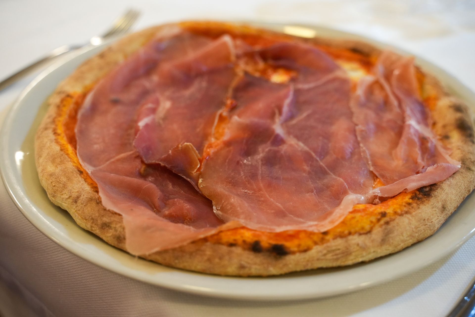 Una pizza con prosciutto sopra è su un piatto bianco su un tavolo.