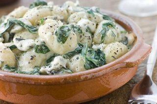 Una ciotola di gnocchi con spinaci e formaggio in salsa cremosa.