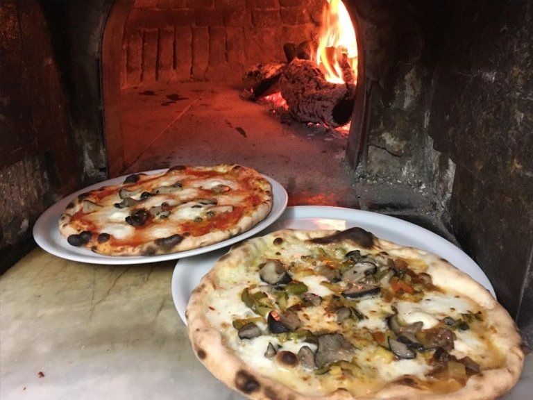 Due pizze sono sedute su piatti davanti a un forno per pizza.