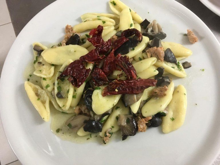 Un piatto bianco condito con pasta e verdure su un tavolo.