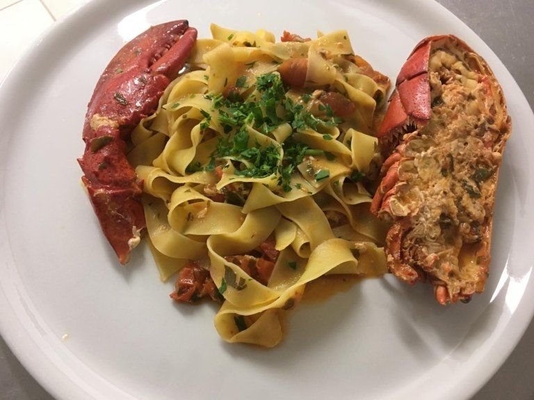 Un piatto bianco condito con pasta e aragosta su un tavolo